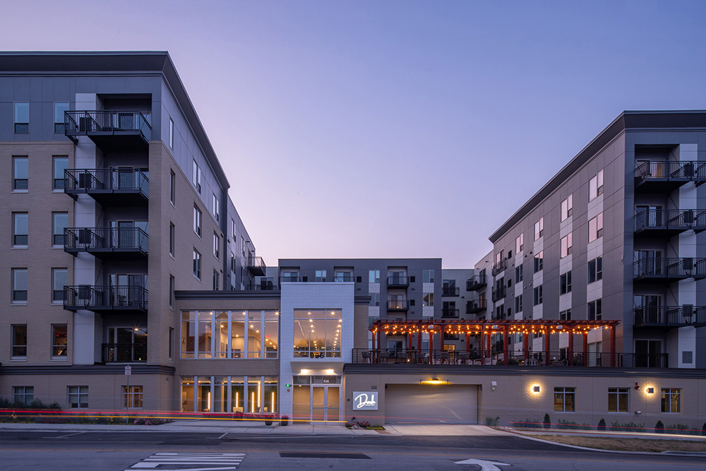 exterior of residential apartment building showing lobby entrance, apartment towers and parking garage entrance with outdoor living area on top at sunset
