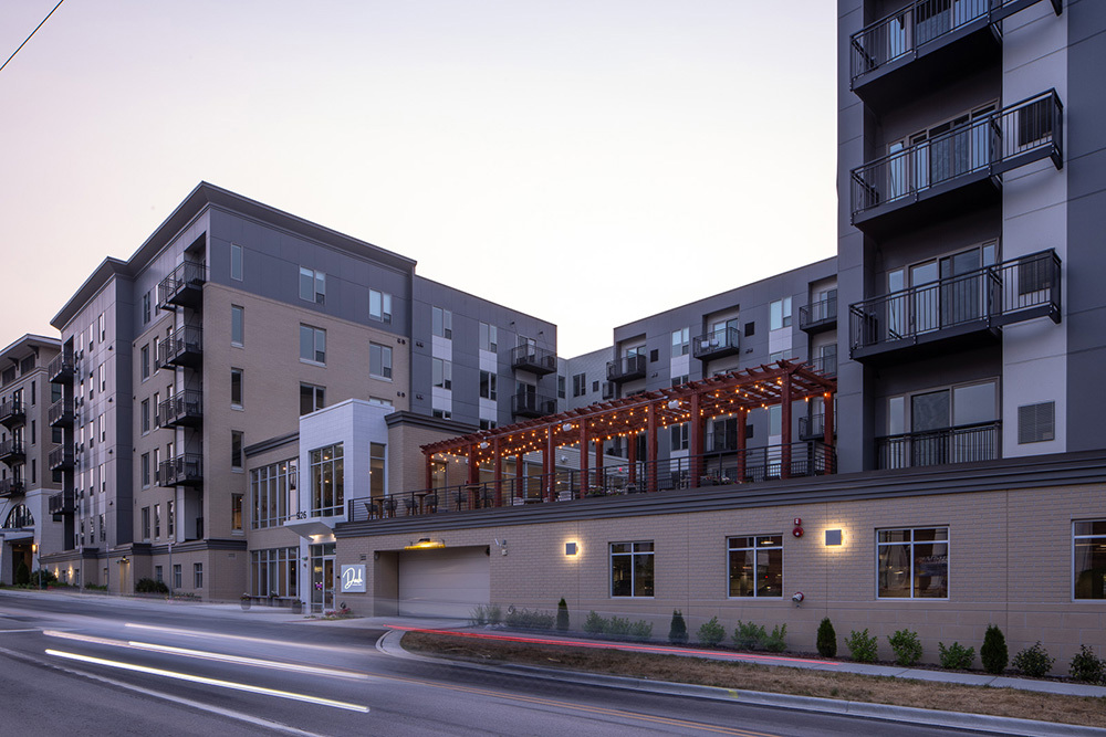street view of the front of an apartment building showing lobby entrance, apartment towers and parking garage entrance with outdoor living area on top