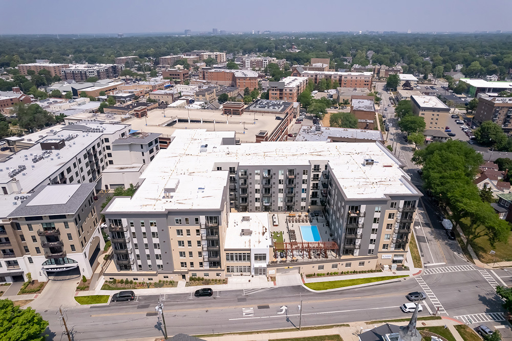 aerial view of residential building from above showing apartment towers and outdoor living area, including pool, on roof of parking garage entrance