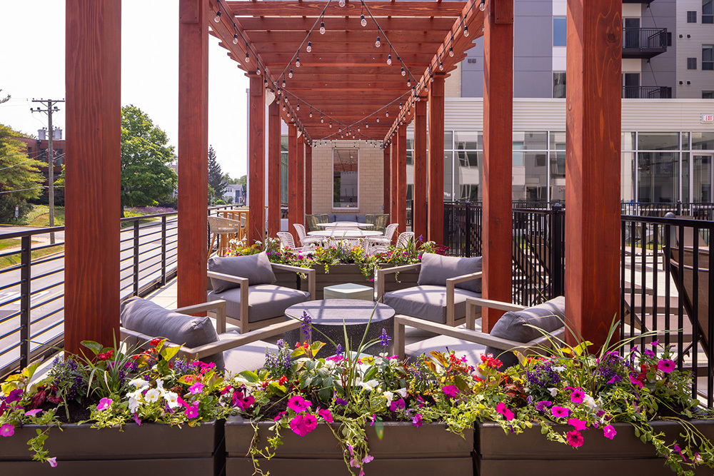 view of rooftop outdoor living area of an apartment building with seating areas under pergola