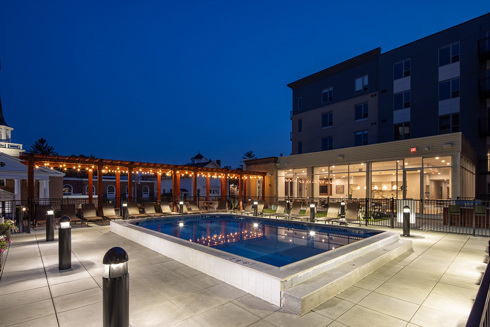 night view of apartment building rooftop outdoor living area with pool in foreground and seating areas and apartment tower in background