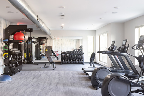fitness center in an apartment building with a row of exercise equipment along an exterior wall with windows