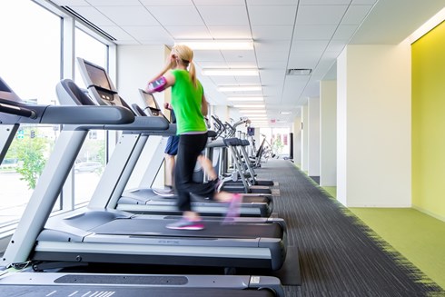fitness center in an office building with rows of exercise equipment along a wall with windows