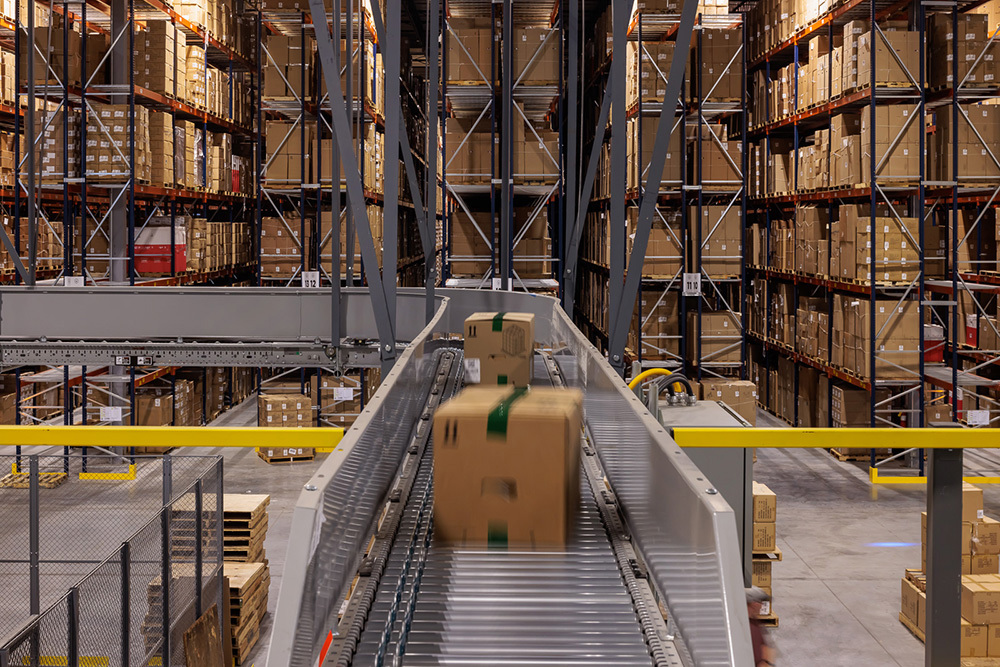 warehouse in an industrial building with boxes on a conveyor belt in foreground and tall shelves filled with boxes in background