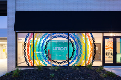 street view of the exterior of an apartment building at night focusing on a colorful, circular design across five windows illuminated by the lobby