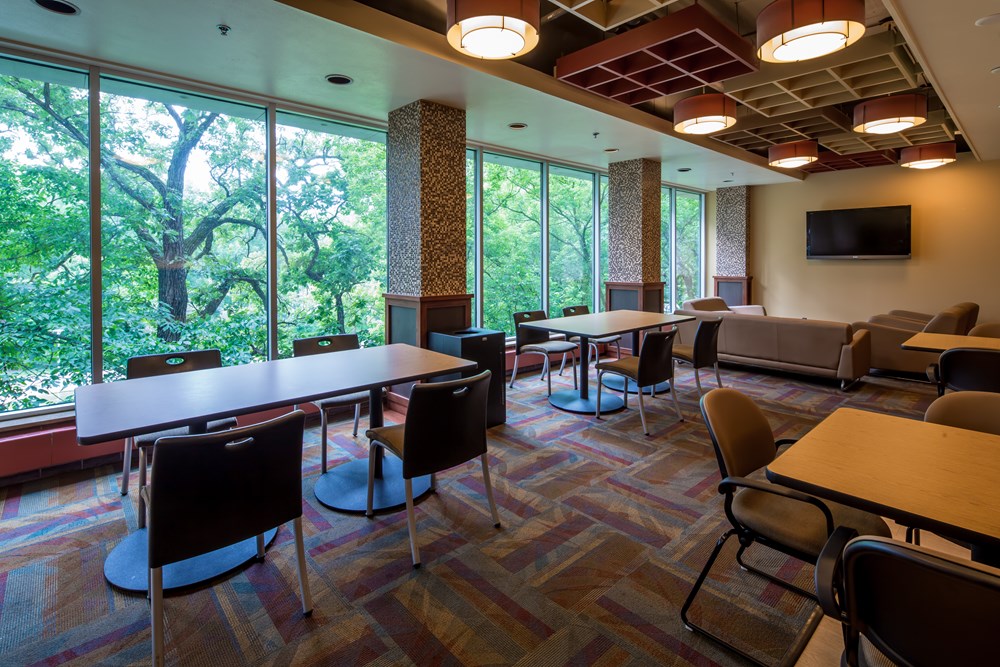 common area in a university dorm with rows of tables with chairs with a wall of windows in the background