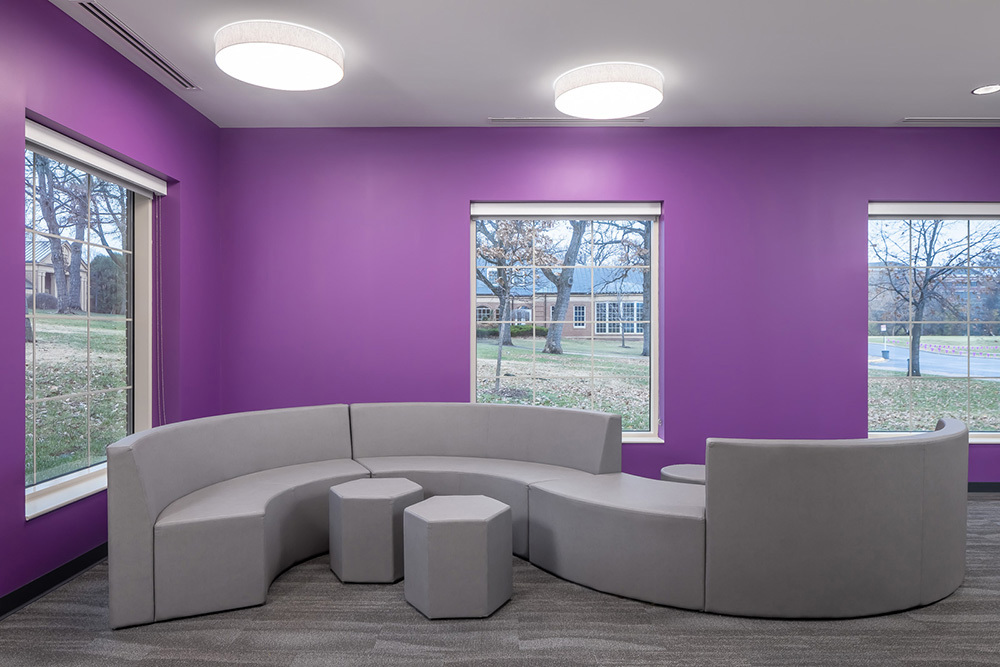 interior of institutional building with curved sectional couch and hexagon ottomans in a room with bright purple walls