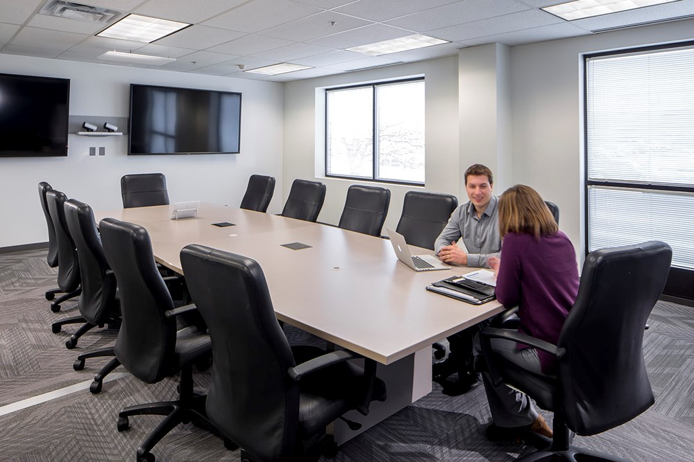 conference room in an office building where a man and woman sit at a large conference table