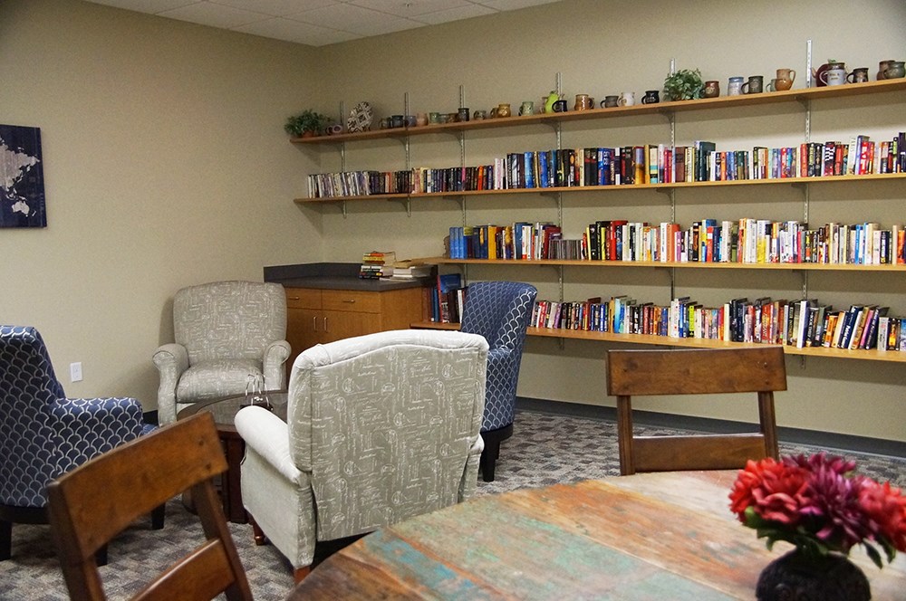 meeting space in an institutional building with a table with chairs and a coffee table with comfy chairs in front of a wall of shelving