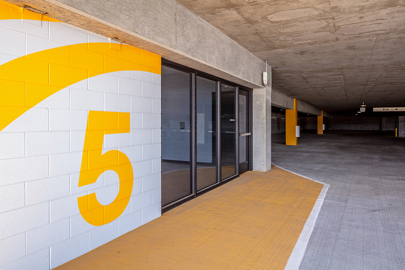 on the left is an entrance to an elevator bank and stairwell in a parking garage with a yellow number 5 painted on the wall and on the right are parking spaces